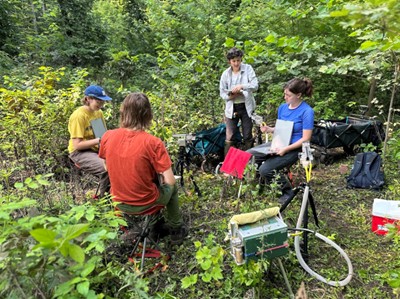 A group of four students next to equipment in a forested area taking measurements.